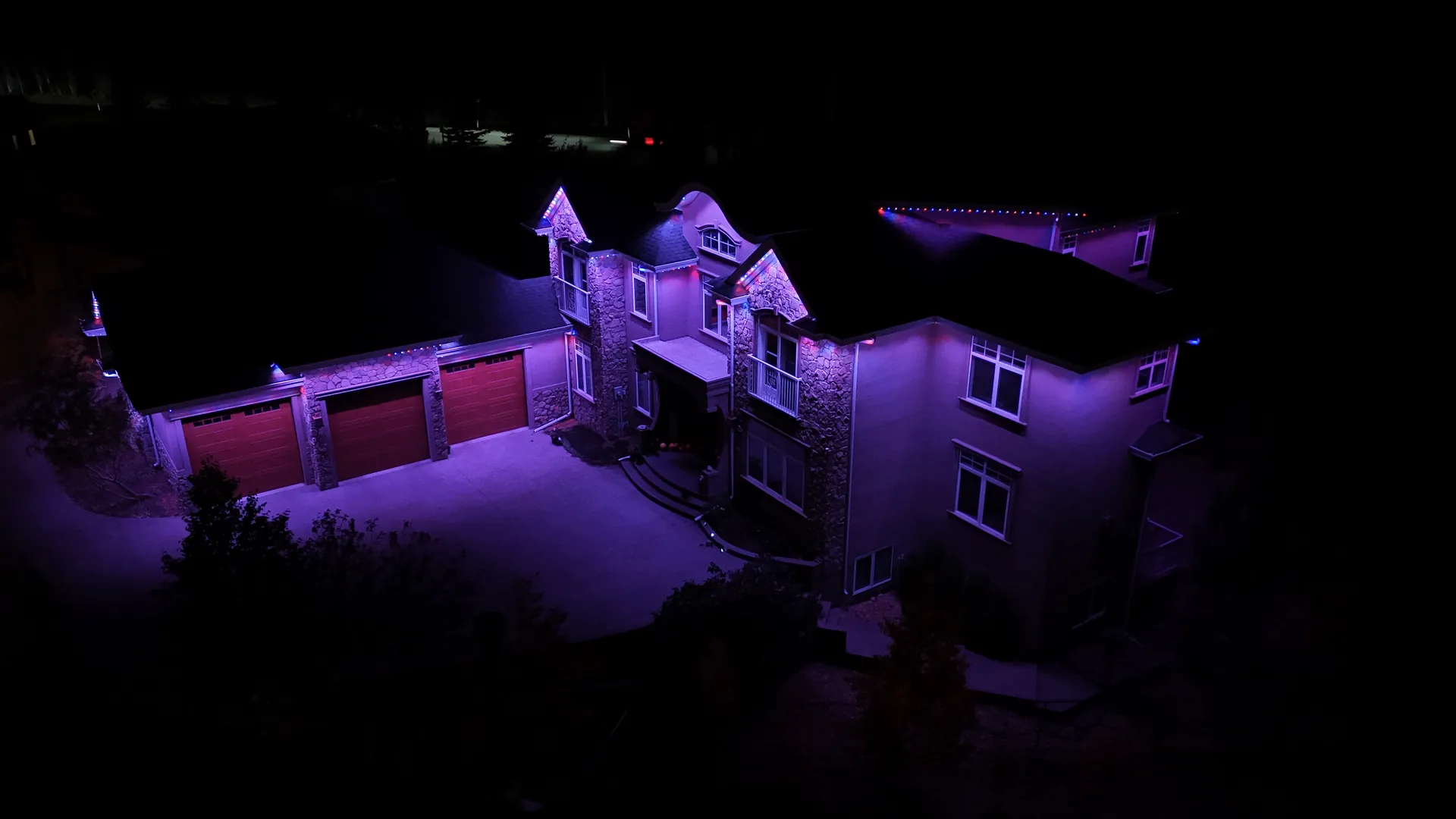 Home with red garage doors lit in purple permanent LED roofline lighting in Edmonton, Alberta